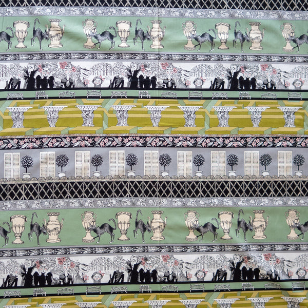 Ghastlie Grounds in Headstone by Alexander Henry Fabrics, 24 inch border stripe panel with topiary urns and long-tailed black cats, a crowd of Ghastlies, garden benches, plinths, shuttered houses and lattice bands in sage green, chartreuse, grey, black and cream